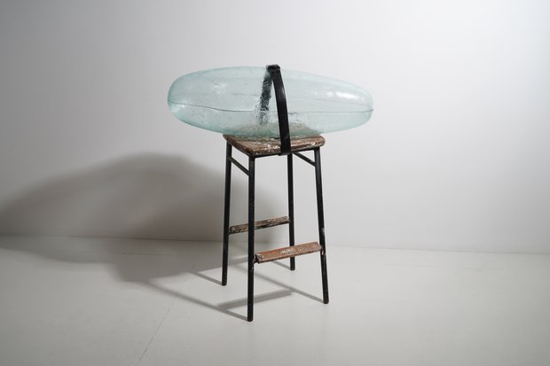 Emma Woffenden: New glass/mixed media works, 2024. Pupae strapped to stool.2024 h.94 x w.80 x d.35 Float glass. hot formed cut and glued. Found stool and belt.