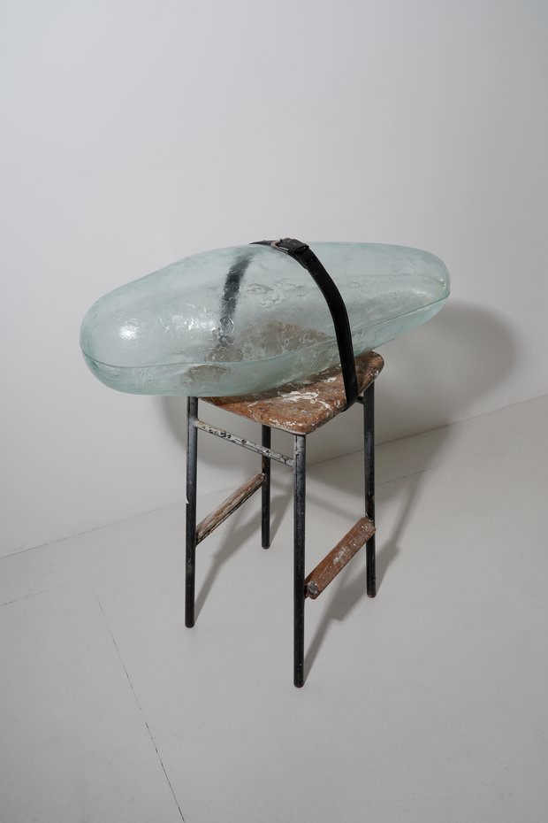 Emma Woffenden: New glass/mixed media works, 2024. Pupae strapped to stool.2024 h.94 x w.80 x d.35 Float glass. hot formed cut and glued. Found stool and belt.