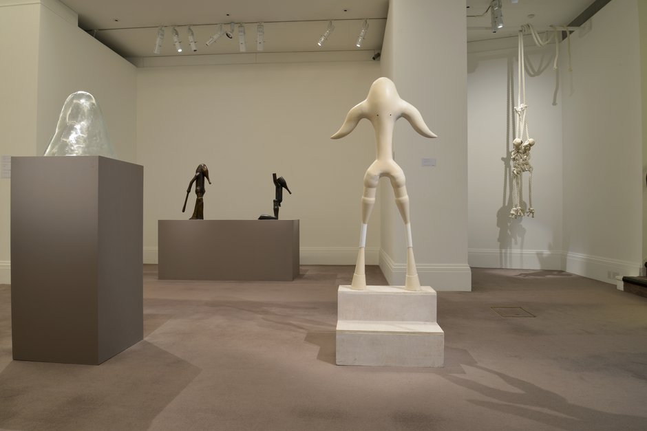 Emma Woffenden: Originals, Sothebys, 2015. Foreground: Figure at Top of Stairs.
jesmonite and wood. Glass head left in image. Trapeeze rope figures background.